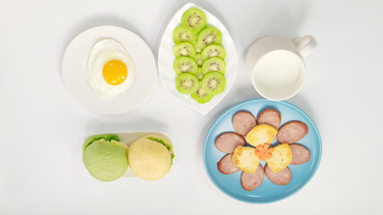 Rich in nutritious breakfast, small hamburger, fried eggs, ham slices, kiwi slices, milk, top view