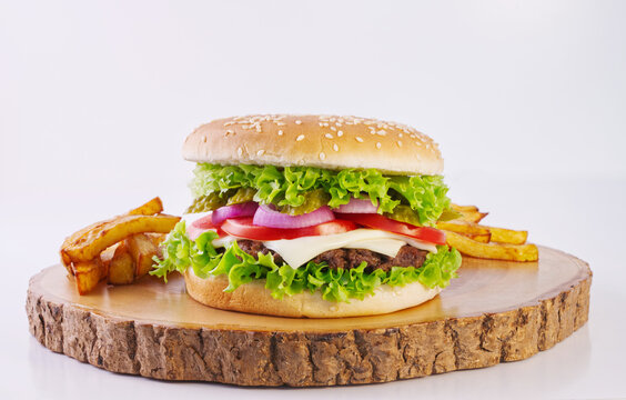 Hamburger with cheese and pickles, french fries on wooden cutting board, delicious fast food, white background