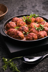 Meat balls with tomato sauce  in a frying pan on a black background.