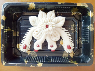Food made from wheat in a shape of a pair of peacocks and a rose, black tray with flower pattern
