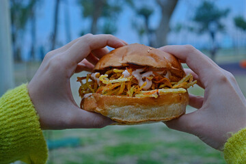 person holding a hamburger with fries with outside background