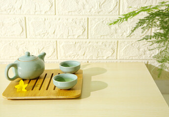 Ceramic tea set on wooden table, potted plant, white marble background, copy space