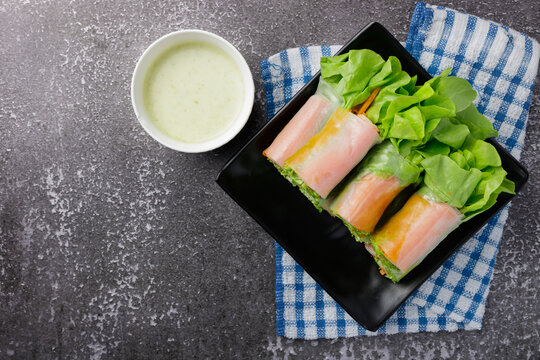 Fresh Salad Spring Roll There Are Many Kinds Of Vegetable, Lettuce, Carrot, Onion, And Crab Stick On Black Dish With Sauce In White Mini Bowl On Gray Stone Background. Top View Photo.