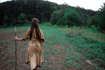 Young native american woman with a spear walking to the forest, indian cosplay, tribal warrior concept, beautiful young girl in indian tribe costume posing with back turned to camera