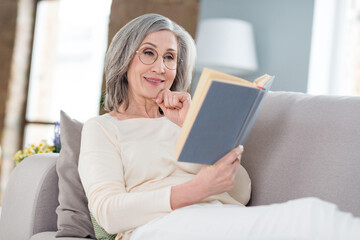 Portrait of attractive focused cheery woman lying on divan enjoying reading interesting book pastime at home house flat indoor
