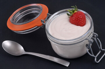 Bocal en verre de crème à la fraise maison avec une fraise fraîche  dessus et une cuillère en gros plan sur fond noir