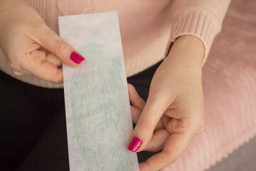 Hair removal wax strips with hair close-up in the hands of a young woman. Body hair removal concept with wax and sugaring at home or spa salon - obrazy, fototapety, plakaty