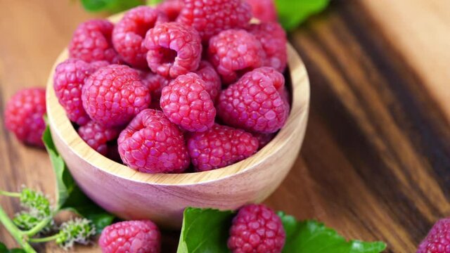Top view Rotate Red Raspberry fruit in wooden bowl on Wooden background, Raspberries with leaves on Wooden background. 4k