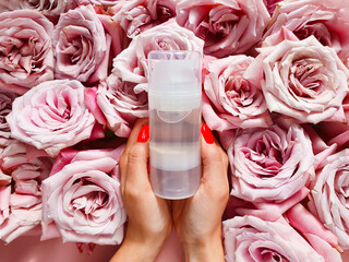 Transparent bottle of intimate lubricant gel, female hands with red nails and pink roses. Intimate...