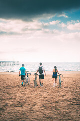 friends seen from behind holding their bikes on the beach at dawn heading out to sea with a bridge in the background. background with copyspace. Free time concept. Concept of sport
