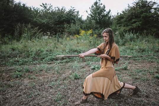 Apache tribe warrior striking with a spear, beautiful young girl in traditional dress posing in the field with a spear, confident woman scout standing with a weapon ready to attack