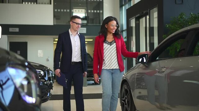 Sales manager car, man agent help client open auto door for african woman to test vehicle Spbd