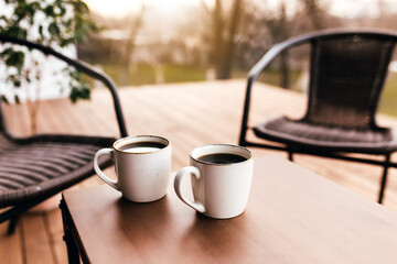 Two cups of coffee on the table on wooden brown terrace during evening sunset