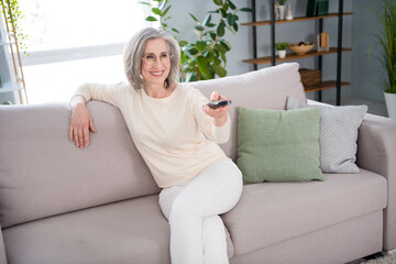 Portrait of attractive cheerful woman sitting on divan resting switching channel spending day at home house indoor