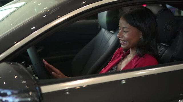 Woman sitting into new car and laughing while shopping in dealership office spbd.