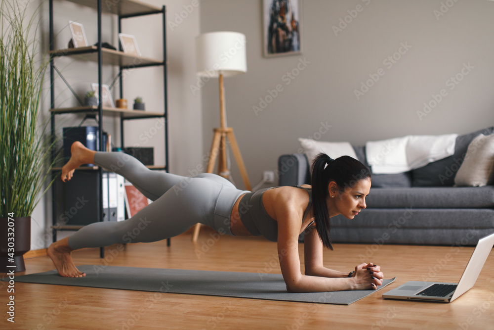 Wall mural young woman practicing yoga online via laptop at home