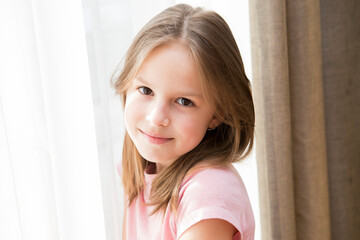 Portrait of an eight-year-old girl in a pink T-shirt in the room
