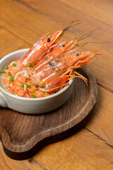 Cooked shrimps served in a white bowl on a wood plate with garlic onion and chili. Sea food.