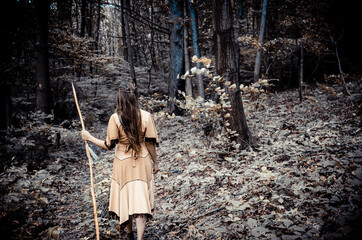 Apache tribe scout looking for tracks in the woods, beautiful native american female warrior looking for footprints in the forest, indian dress concept