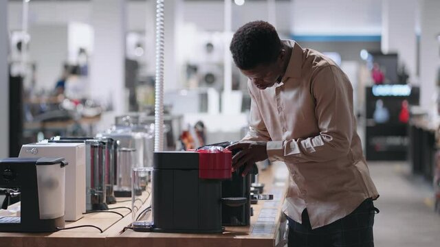 black man is choosing coffee machine in home appliance store, young guy is examining exhibition sample in hardware store
