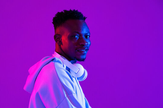 Young Handsome African Man With Headphones In Purple Futuristic Neon Light Studio Background