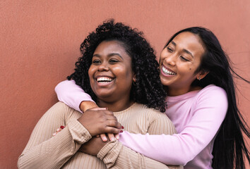 Happy Latin friends having fun embracing while standing against red wall - Young women lifestyle...
