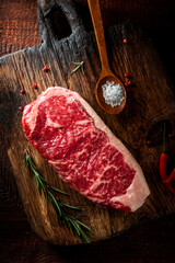 Raw striploin steak (New York) of beef on a seasoning board. Rustic style with wooden old background