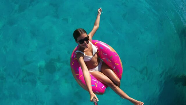Holidays Travel Vacation Fun. Woman in float donut doing selfie video with selfie stick in turquise perfect water in donut inflatable ring floating on ocean.
