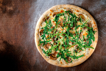 A whole pizza with arugula, cheese, porcini mushrooms and truffle oil. Recipe Italian pizza on a wooden brown background