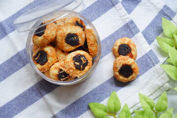 a jar of thumbprint cookies with jam and grated cheese in white background