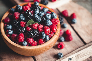 Ripe blackberries with leaves in a bowl on a wooden board on a dark background