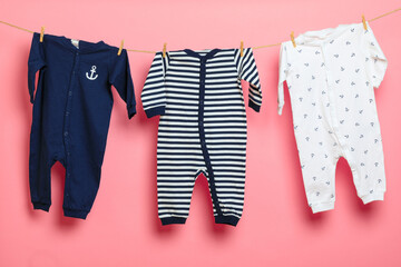 Baby clothes on a clothesline on pink background .