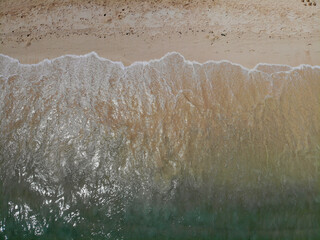 Bird's eye view drone shot of a sandy shoreline on the Island of Oahu, Hawaii during golden hour. A beautiful beach with crystal clear water and blue skies.