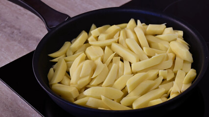 Closeup raw potatoes sliced for homemade French fries in frying pan at kitchen stove. Cooking of fried potatoes in skillet top view