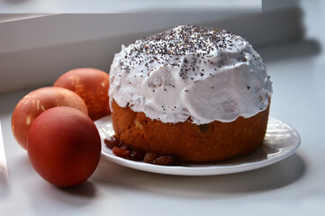 Easter cake is watered with white glaze and sprinkled with poppy seeds on top. Three brown chicken eggs dyed with onion skins. Close-up photo on a light blurry gray background. Home cooking 