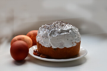 Easter cake is watered with white glaze and sprinkled with poppy seeds on top. Three brown chicken eggs dyed with onion skins. Close-up photo on a light blurry gray background. Home cooking 