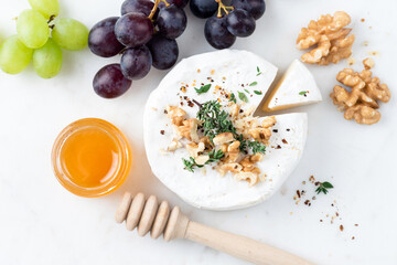 Camembert cheese with walnuts, honey and grapes on a white marble cheese board, table top view appetizer