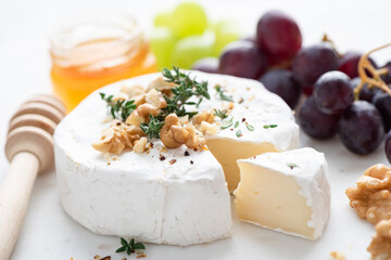 Brie or camembert cheese with grapes, walnuts and honey on white marble cheese board