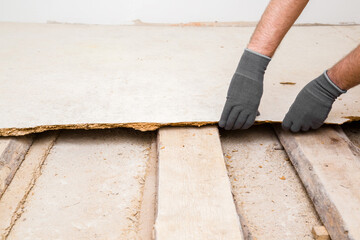 Young adult man hands in protective gloves breaking old wooden floor. Closeup. Preparing for repair...