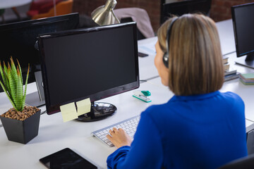 Asian businesswoman sitting in front of computer wearing headset having video call