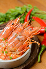 Cooked shrimps served in a white bowl on a wood plate with garlic onion and chili. Sea food.