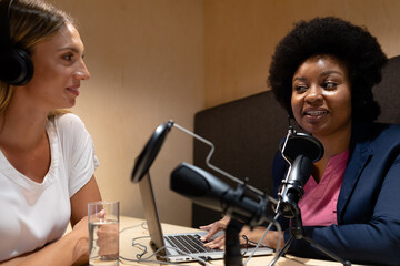 Diverse female business colleagues wearing headphones in discussion speaking to microphones