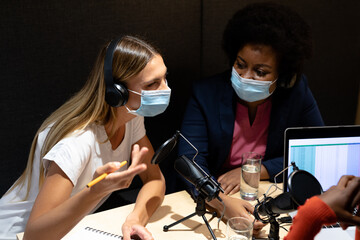 Diverse group of female business colleagues wearing masks in discussion speaking to microphones