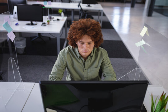 Mixed race businessman sitting in office in front of computer near sneeze shield