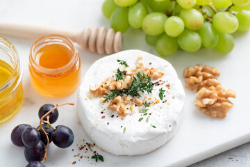 Whole camembert or brie cheese on a cheese platter served with grapes, honey, walnuts and thyme