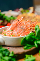 Cooked shrimps served in a white bowl on a wood plate with garlic onion and chili. Sea food.