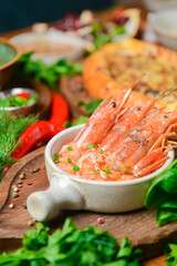 Cooked shrimps served in a white bowl on a wood plate with garlic onion and chili. Sea food.