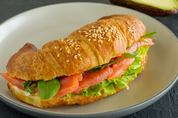 croissant sandwich with salmon, ricotta cheese and arugula on a plate on a dark background. Side view close up