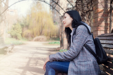 Portrait of beautiful brunette girl in plaid coat sits on a bench in the park