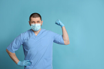 Fototapeta na wymiar Doctor with protective mask showing muscles on light blue background, space for text. Strong immunity concept